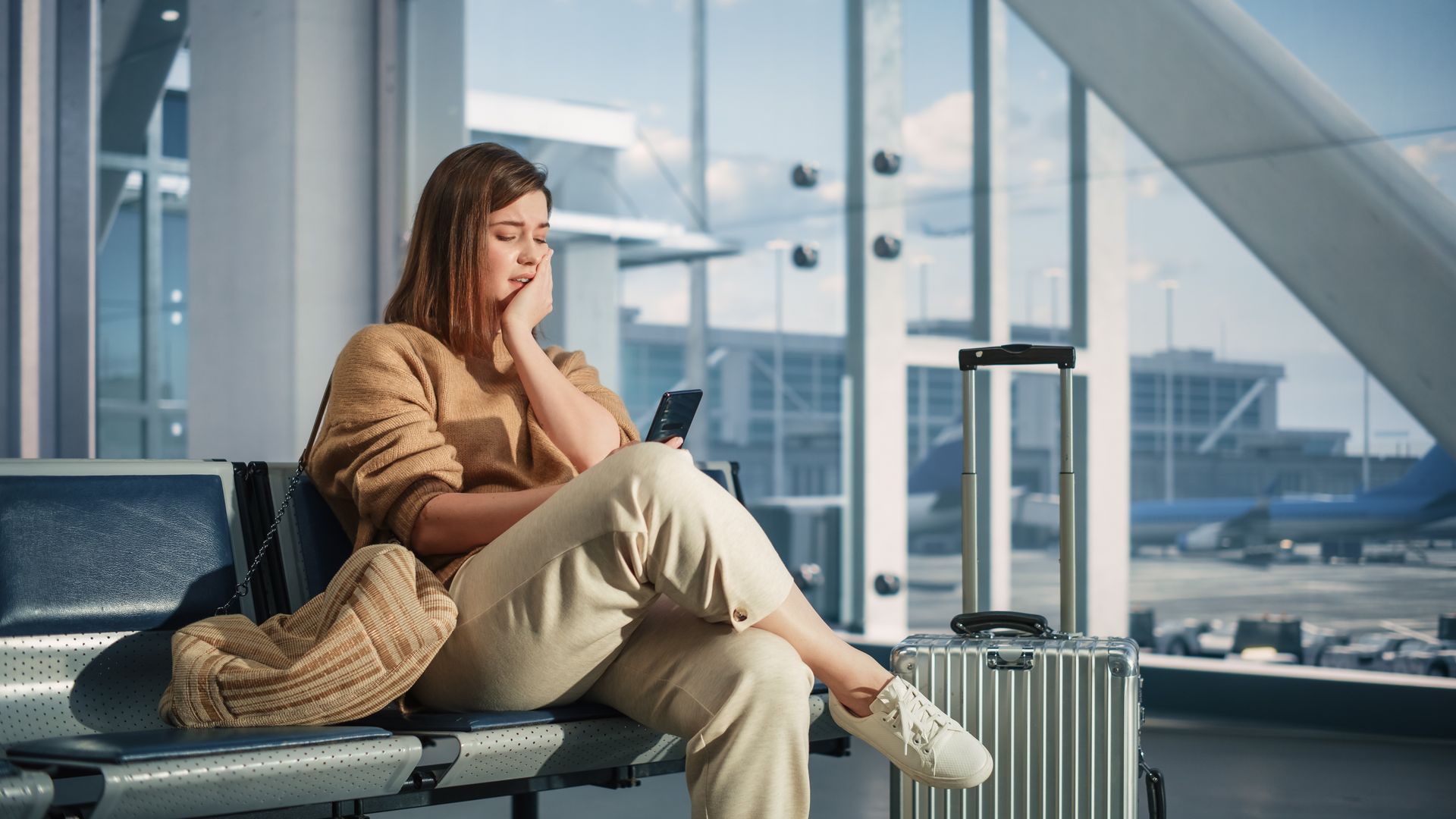 Frau sitzt am Flughafen und schaut traurig