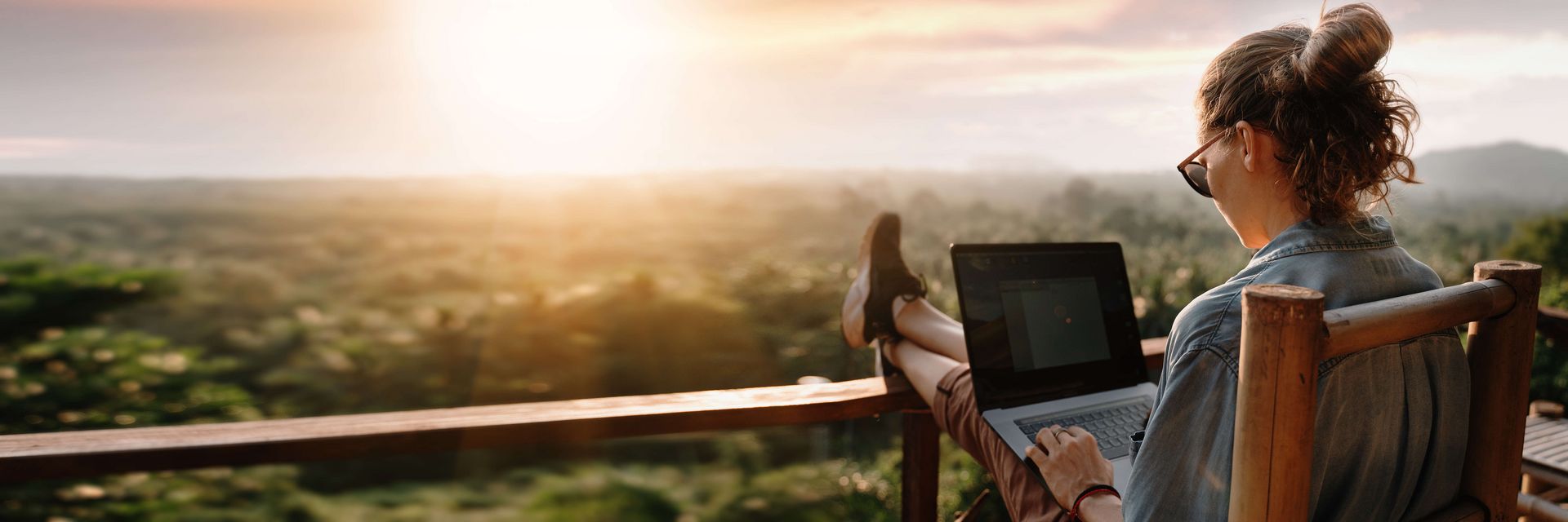 Junge Frau mit Laptop auf Terrasse im Sonnenuntergang